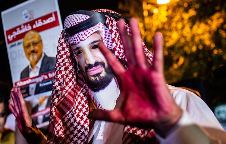 A protester wears a mask depicting Saudi Crown Prince Mohammed Bin Salman with painted hands next to people holding posters of Saudi journalist Jamal Khashoggi during the demonstration outside the Saudi Arabian consulate in Istanbul on October 25, 2018. (AFP/Yasin Akgul)